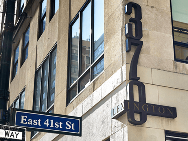 The image shows a street corner with a building featuring a sign that reads  LEXINGTON  and the address  175 EAST 41ST ST.  There is also a sign for an establishment named  East 41st Street  on the ground floor of the building. The photo captures the facade of the building, including its windows and architectural details, with a clear sky in the background.