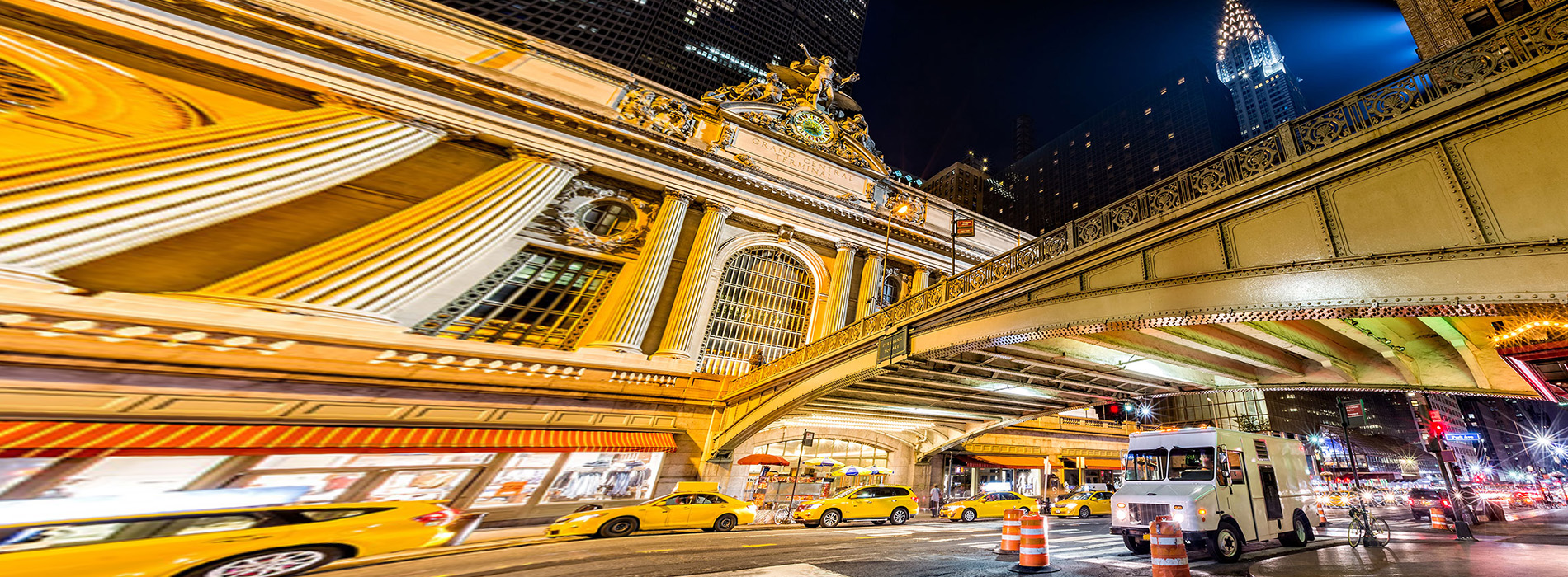 The image depicts a vibrant night scene of a city street, characterized by bright lights and the blurred motion of vehicles, with a distinctive perspective that creates an abstract, tunnel-like effect.